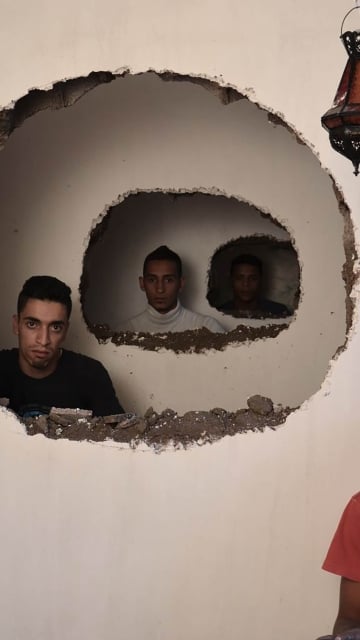 men in different rooms seen through holes in the wall