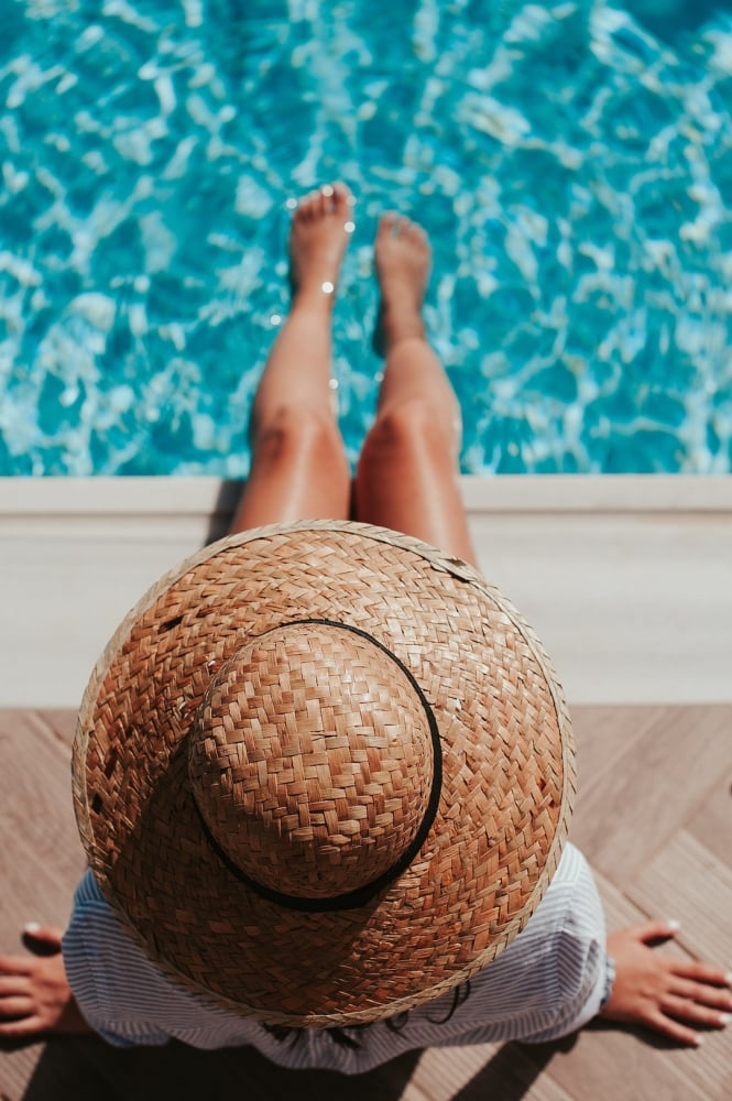 Lady wearing a straw sunhat with feet in swimming pool