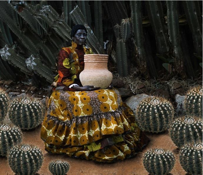 a woman sitting with a clay pot surrounded by cacti 