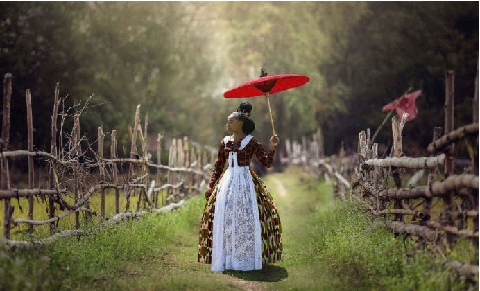 a woman in the country with a red umbrella blocking the sun
