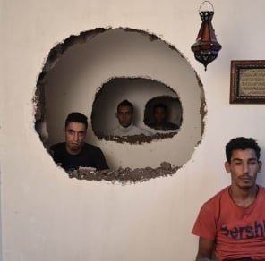 men in different rooms seen through holes in the wall