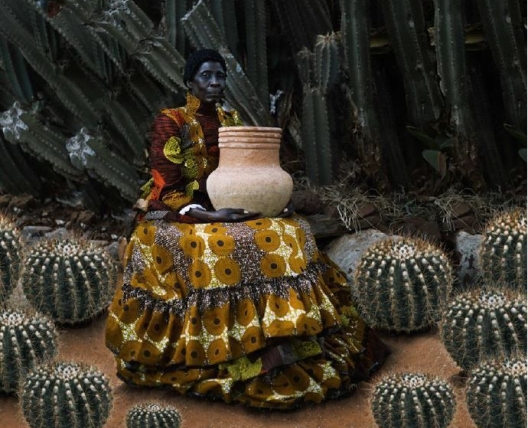 a woman sitting with a clay pot surrounded by cacti 