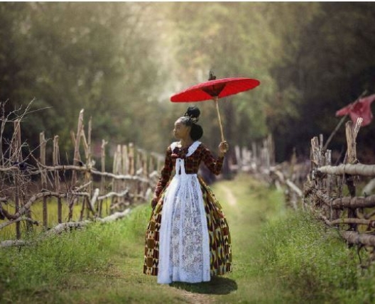 a woman in the country with a red umbrella blocking the sun